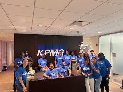 Students in blue KPMG shirts in front of KPMG logo